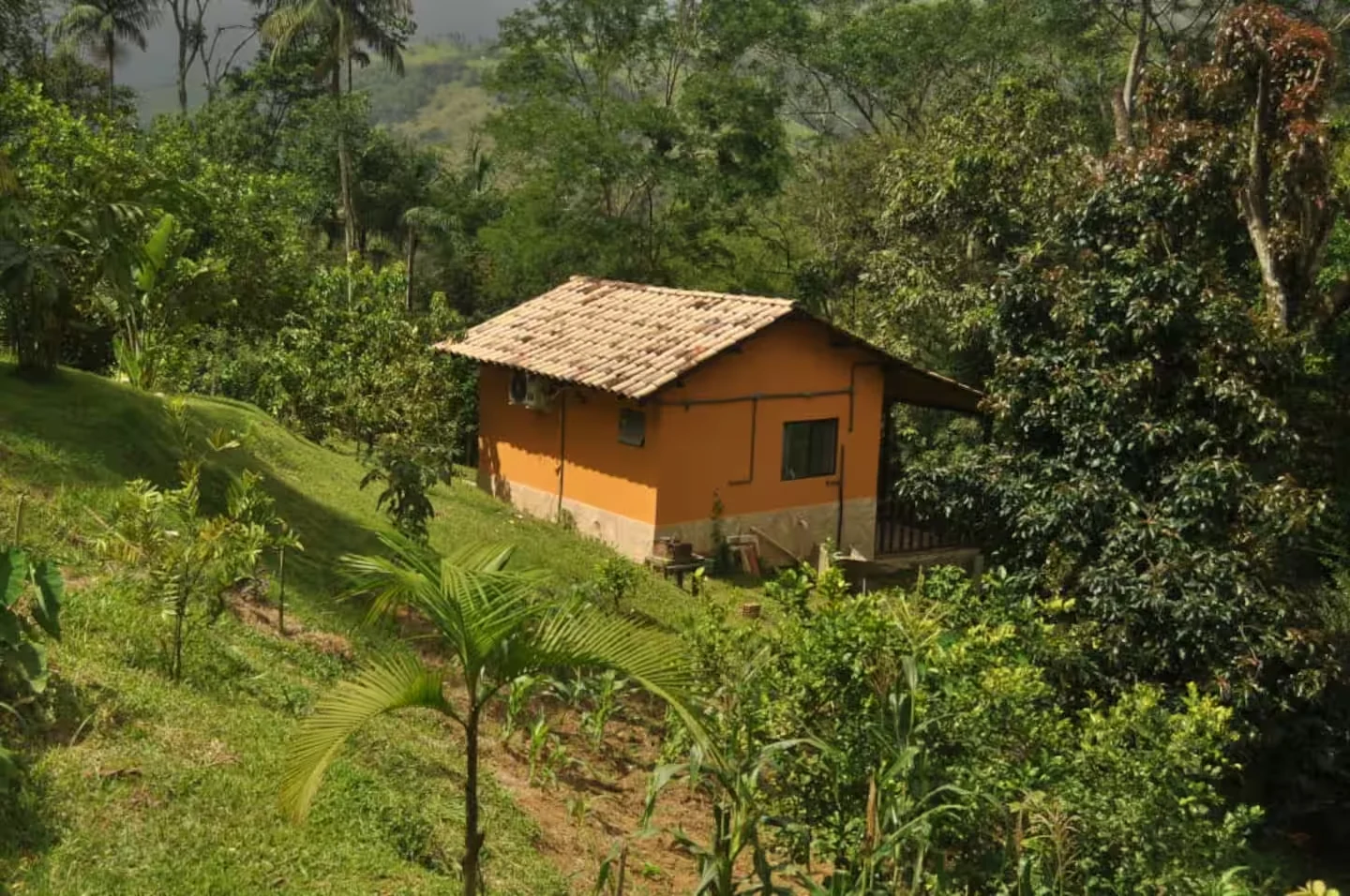 Casinha Calêndula em meio à encosta verde, com telhado de barro e vista para a serra