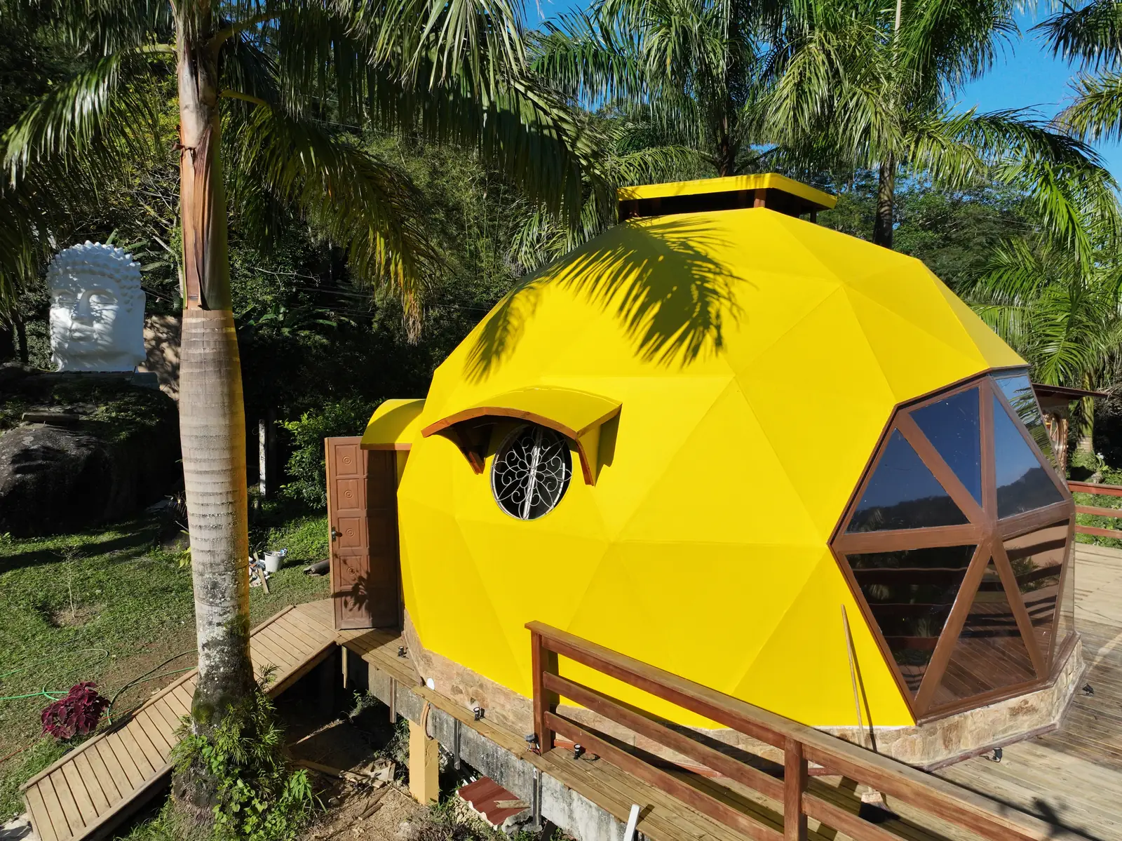 Domo Gaturamo Real, em amarelo, com deck de madeira entre as palmeiras
